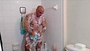 muscular guy soaps oiled body in shower